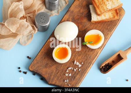 Wooden board with soft boiled eggs and bread slices on blue background Stock Photo