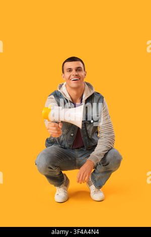 Young man with megaphone on yellow background Stock Photo