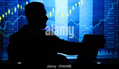 Silhouette of a businessman analyzing stock market data and financial charts on a laptop, investment and trading, this image investment trading and ec Stock Photo