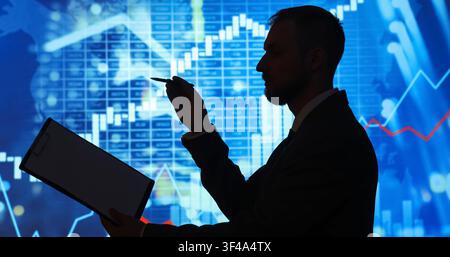 Businessman silhouette analyzing financial data and stock market charts on a blue digital screen background Stock Photo