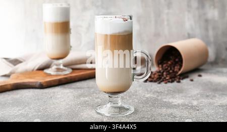 Layered latte macchiato in a tall glass with frothy milk and coffee beans on a gray background, Roasted coffee beans are spilled from a paper containe Stock Photo