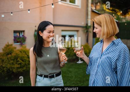 Two happy multi ethnic women toasting rose wine at garden party Stock Photo
