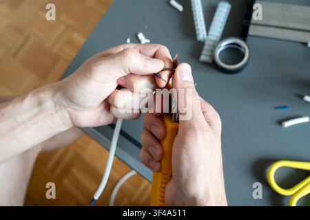 Using a utility knife to prepare cable for a ceiling light installation Stock Photo