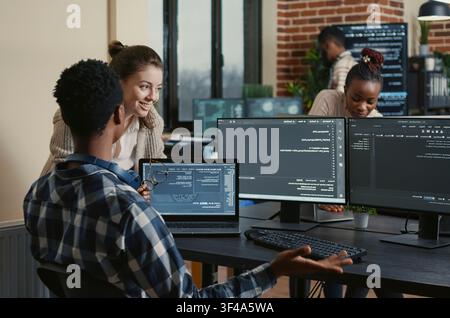 Software developers celebrate a successful code compile with a high five at an office desk, surrounded by screens showing programming and algorithms. Stock Photo