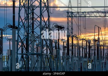 An electrical substation featuring steel towers, transformers, and power lines against a golden sunset sky in Villa Hayes, Paraguay. Stock Photo