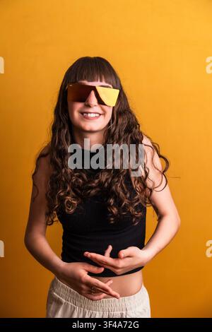 Woman dancing wearing trendy sunglasses on yellow background Stock Photo