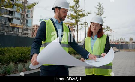 Two contractors civil engineers discuss blueprint city buildings plan project electrical maintenance looking at paper partnership teamwork Stock Photo