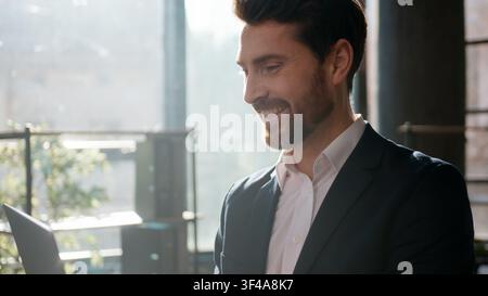 Successful Caucasian business man working on laptop in office sunlight smiling confident male businessman entrepreneur manager leader typing online Stock Photo