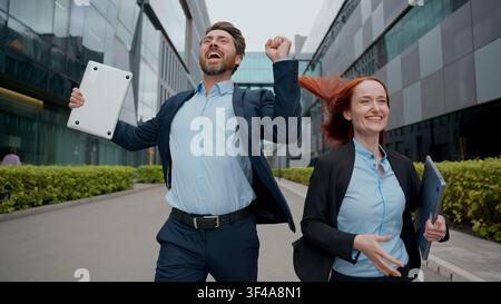 Excited two Caucasian people business colleagues woman man run in city celebrate success good result achievement end work day financial winning Stock Photo