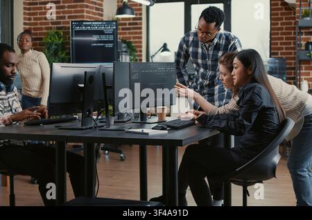 Programmers collaborating on group project compiling algorithm for new cloud computing user interface on computer screens, mixed team of software engineers brainstorming ideas looking at running code. Stock Photo