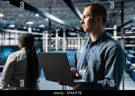 Team of data center system administrators deploying tools to reduce downtime using devices. Server farm colleagues monitoring thermal performance of hardware using software on laptop Stock Photo