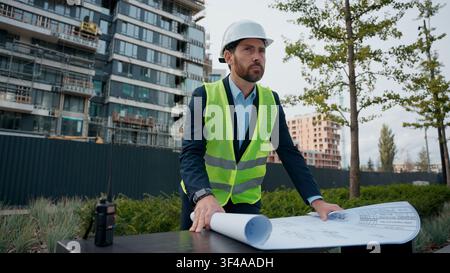Caucasian man builder engineer in helmet looking plan blueprint building project urban city development business male businessman in safety hardhat Stock Photo