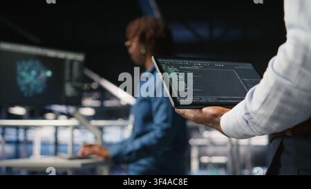 Close up of data center admin using tablet to reviewing machine learning code dashboards. Server farm IT expert using device to monitor AI infrastructure performance, Stock Photo