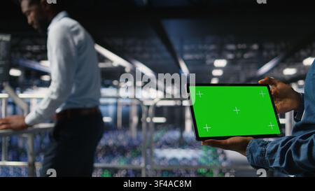 Close up of engineer using green screen mockup tablet in data center to update servers tech, configuring equipment. Server room admin reviewing hardware analytics on chroma key device, Stock Photo