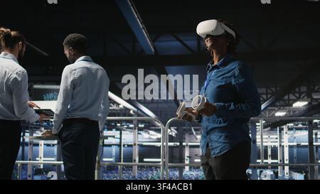 Engineer on data center industrial platform analyzing performance outputs using virtual reality tech. Server hub colleagues finetuning server rig configurations using VR headset tech, Stock Photo