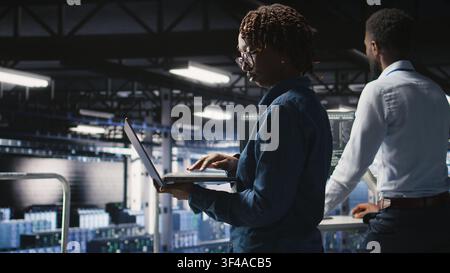 Data scientist in server farm reviewing neural network code and LLM visualization dashboards. IT expert walking on data center industrial platform, monitoring AI system performance, Stock Photo