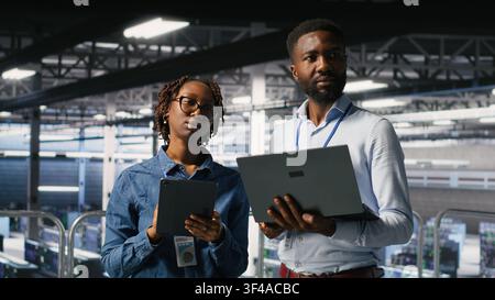 Data center admins running diagnostics on equipment using system monitoring tools to identify errors, doing brainstorming. IT experts work together to prevent failure and minimize downtime Stock Photo