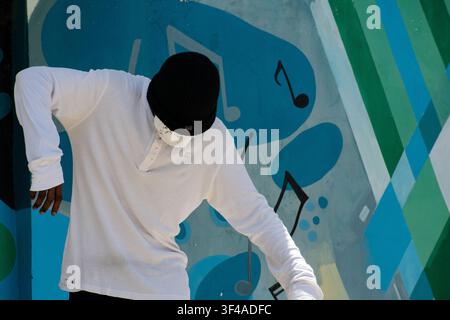 Ciego de Avila, Cuba - July 19, 2026: Young performer wearing a beanie and mask dancing in front of a musical mural at the zoo. Stock Photo