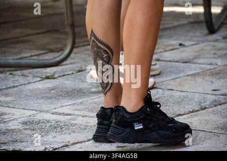 Close-up of a person's legs with an ornate mandala leg tattoo wearing black sneakers at the Ciego de Ávila Zoo, Cuba - July 19, 2026 Stock Photo