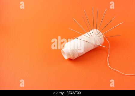 needles and thread isolated orange color background Stock Photo