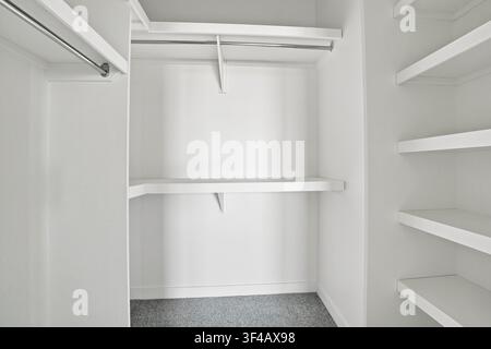 White closet interior features empty shelves and hanging rod. Speckled flooring adds subtle texture to the space. Minimalist design creates clean, unc Stock Photo
