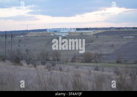 Modern industrial building surrounded by open fields and rolling countryside under a dramatic cloudy sky. Stock Photo