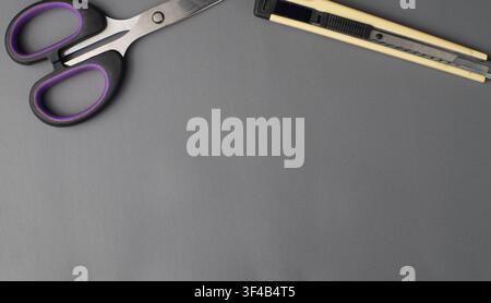 Scissors and cutter placed on the edge of a gray desk background, suitable for office supplies, craft tools, school stationery, workspace Stock Photo