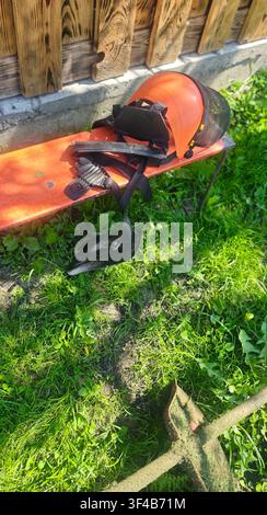 Safety helmet with mesh face shield and shoulder harness for brush cutter on wooden bench in home garden Stock Photo