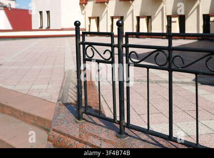 Forged iron railing granite stairs terrace. Vintage metal decorative fence on polished red granite step with blurred pavement and historic building Stock Photo