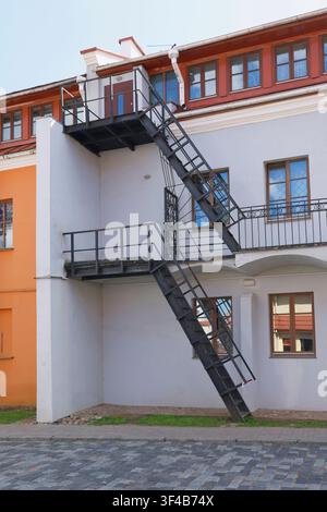 Industrial metal fire escape stairs building facade. External black iron emergency staircase structure on old renovated house wall architectural Stock Photo