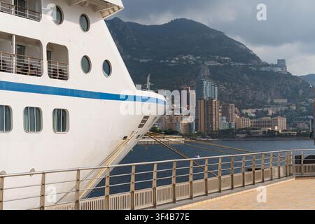 Large white luxury cruise ship moored at port pier with scenic view of coastal city and mountains in Monaco on French Riviera. Stock Photo
