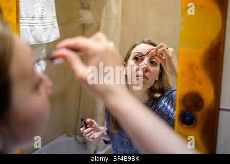 Woman focusing on her reflection while applying cosmetic mascara to eyelashes Stock Photo
