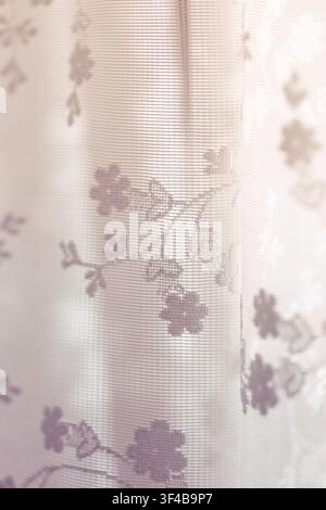 Delicate floral sheer curtain glowing in soft natural morning light, featuring fine mesh texture, gentle folds, and a warm, airy atmosphere Stock Photo