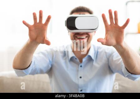 Young man wearing virtual reality glasses, sitting on sofa Stock Photo