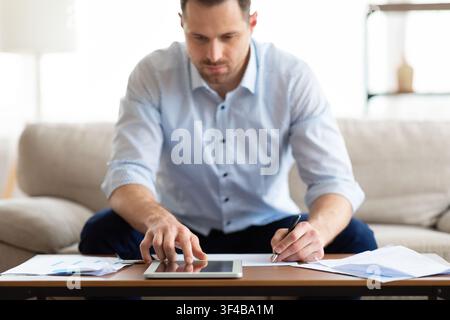 Man using tablet at home and writing notes Stock Photo