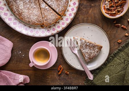 Delicious nut cake slice with espresso and scattered pecans on wooden table Stock Photo