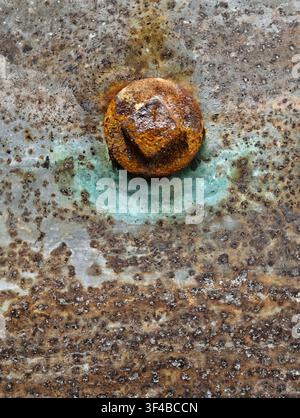 Closeup of rusty metal plate showing circular corrosion pit, peeling oxidation, and rough pitted patina in gray, tan, and orange tones, with worn surf Stock Photo