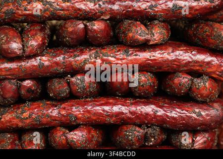 Macro full frame shot of dry cured smoked sausages and mini salami coated in black pepper and spices, tightly stacked in rows. Rich meat texture and f Stock Photo