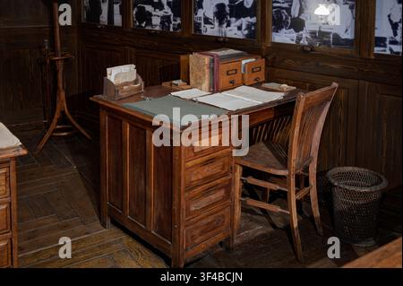Vintage wooden desk and chair in a dark classic office with old books, documents, folders, and retro wooden interiors. Stock Photo