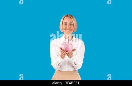Money savings. Portrait of mature businesswoman holding piggybank on blue background Stock Photo