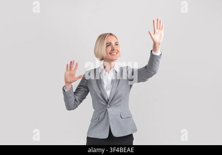 Attractive entrepreneur touching virtual screen on light grey studio background, mockup for design Stock Photo