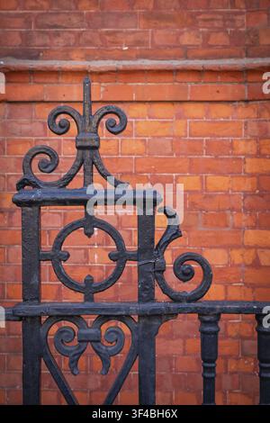 Detail, black ornate wrought iron fence in front of a brown-red brick wall, Chelsea, London, England, Great Britain, Great Britain Stock Photo