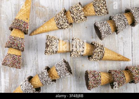 Ice cream cones decorated with nuts and sprinkles on rustic wood Stock Photo
