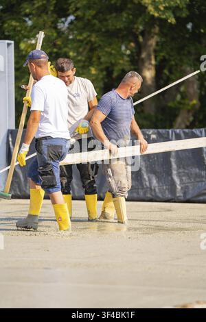 Three construction workers with yellow boots smoothing concrete on a construction site, Parkhausbau, Calw, Germany Stock Photo