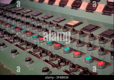 Detailed view of a vintage complex industrial control panel featuring rows of rotary switches, knobs, and colored push buttons. Stock Photo