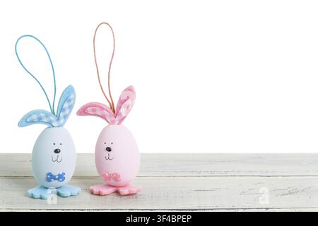 Two decorative Easter eggs with bunny ears, one blue and one pink, placed on a rustic wooden table with a clean white background Stock Photo