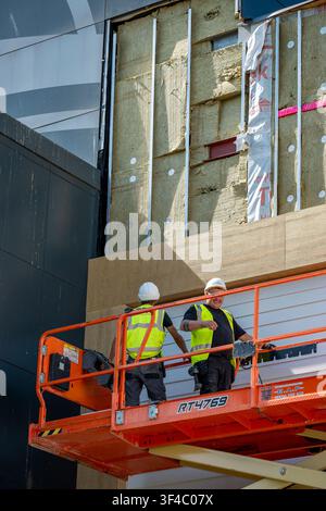 Construction workers using a scissor lift or cherry picker top access building to fit replacement panels and cladding. Stock Photo