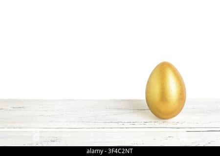 A shiny golden egg placed on a rustic wooden table against a clean white background, highlighting its smooth surface and vibrant color Stock Photo