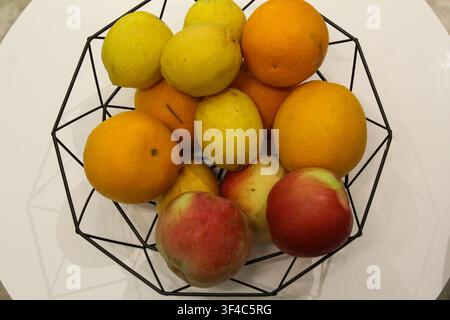 Fresh oranges, lemons and apples arranged in a modern black wire fruit basket on a white background. Healthy food concept. Stock Photo