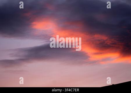 Fiery orange and pink clouds glowing beneath dark storm clouds, creating a dramatic and colorful sunset sky. Stock Photo